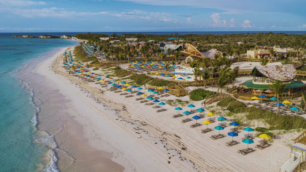 Aerial view of a beach resort, showcasing sandy shores, turquoise waters, and lush greenery surrounding the property.