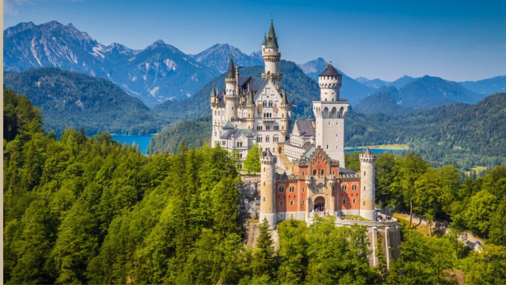 Neuschwanstein Castle in Germany, a fairy-tale structure surrounded by lush forests and mountains under a clear blue sky.