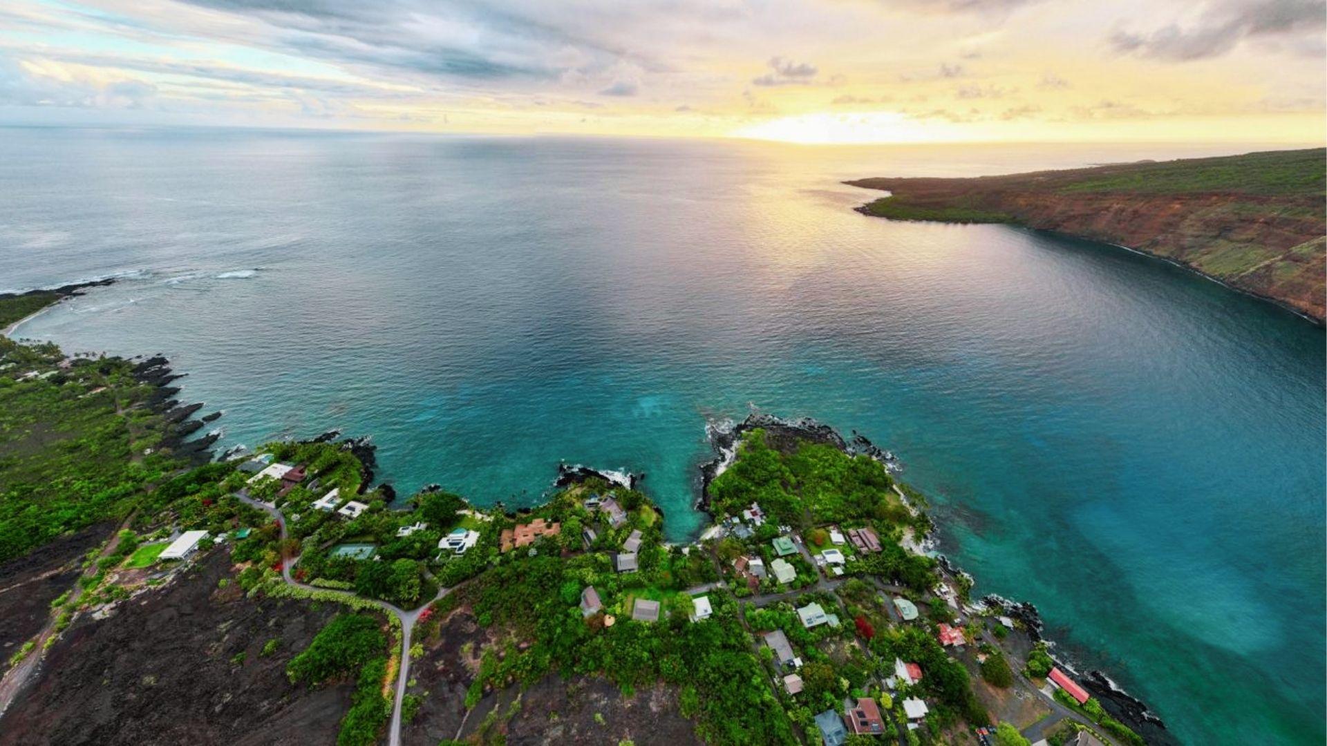Aerial sunset over a coastal Hawaii neighborhood with volcanic rock shoreline and calm bay.