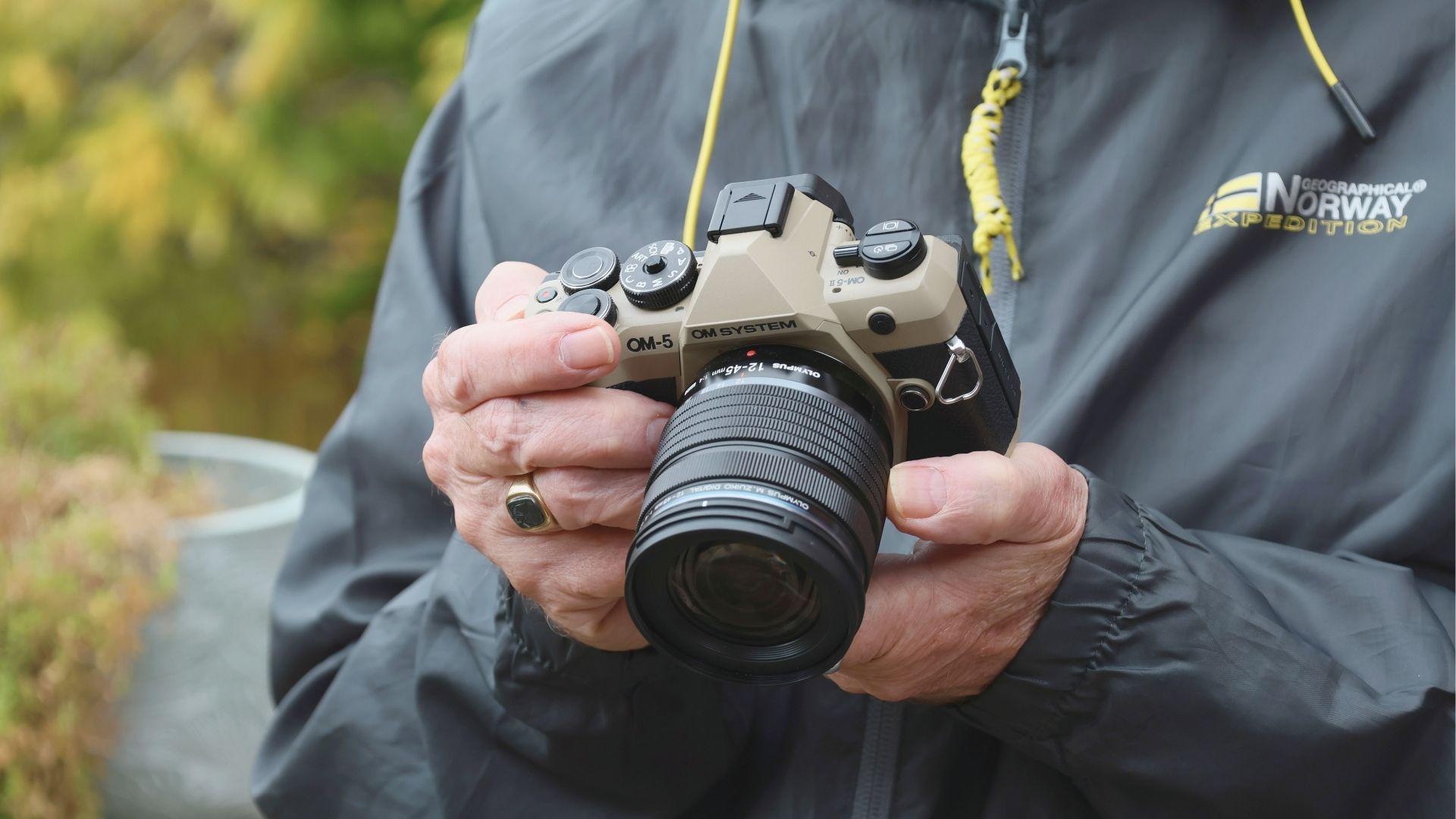 Close-up of a weather-sealed mirrorless travel camera held by a hiker in a rain jacket