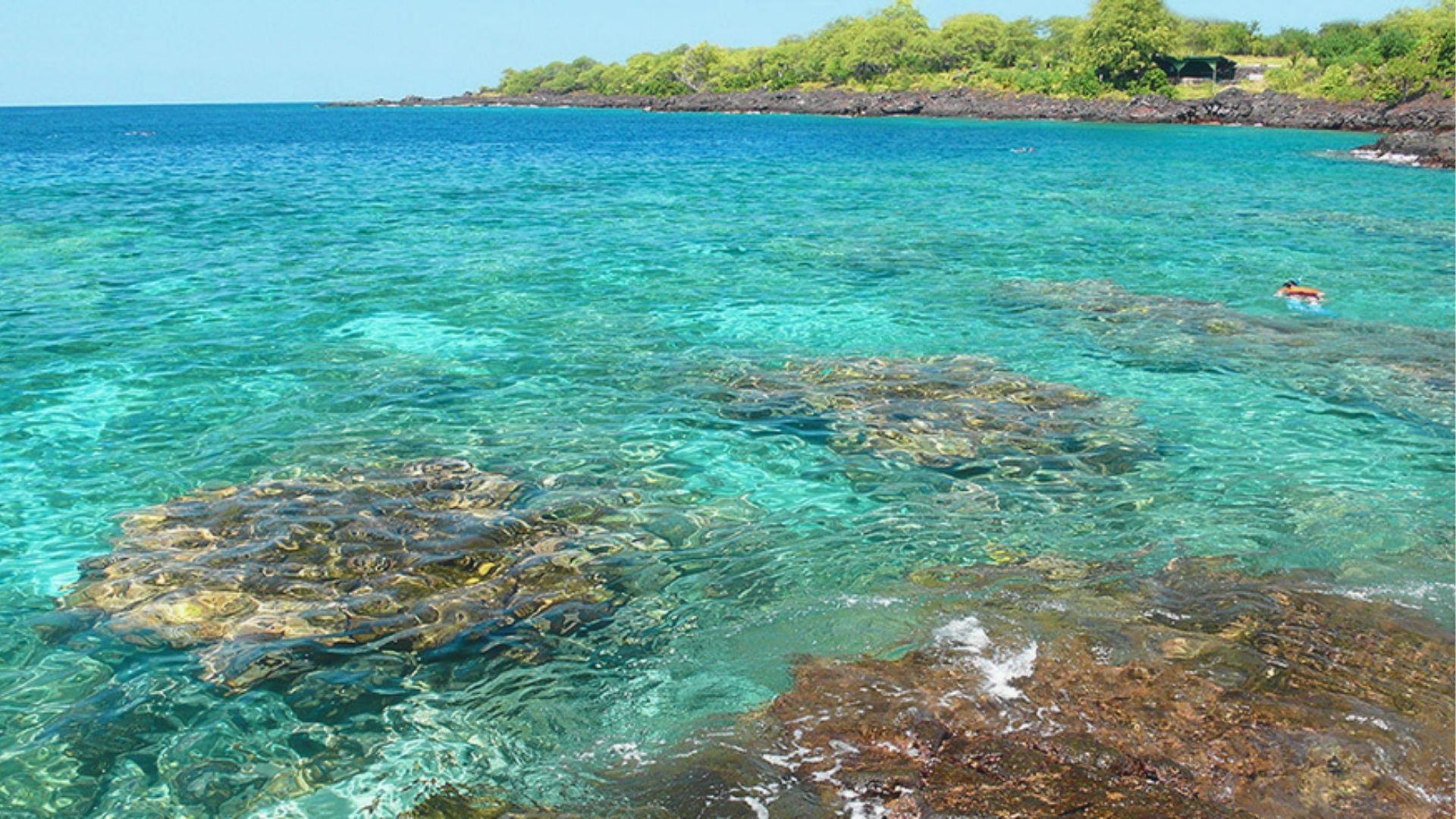 Clear turquoise water over shallow coral heads with a snorkeler in the distance.