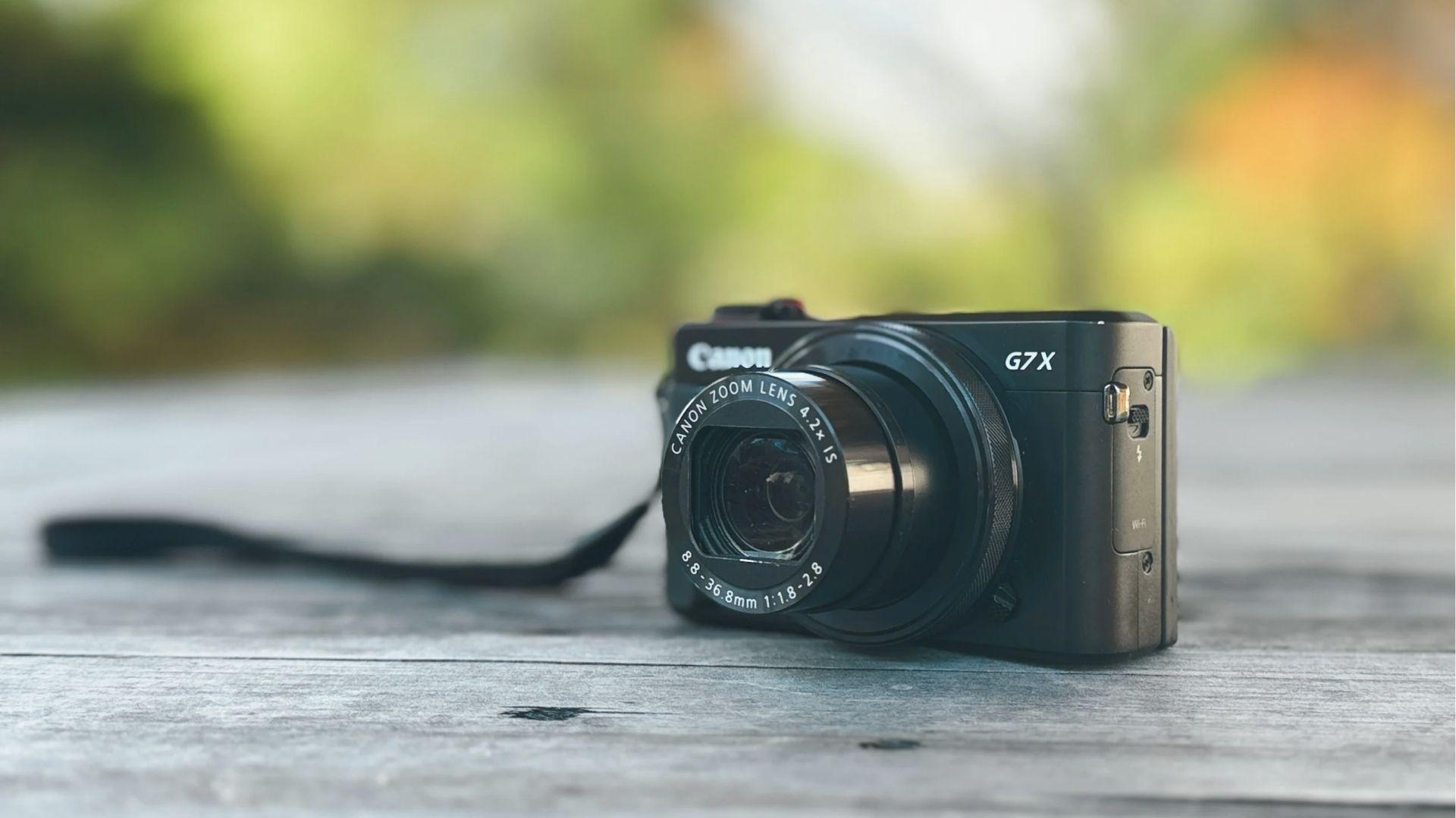 Black Canon G7X compact vlogging camera on weathered wood table, lens extended