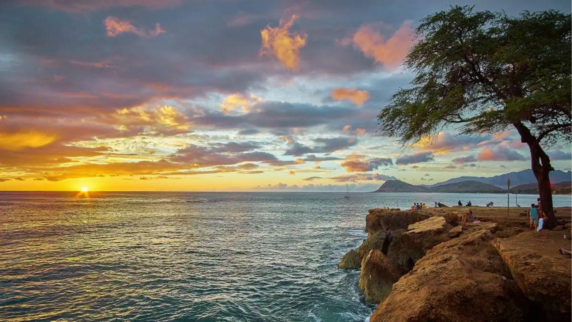 Sunset over the ocean from rocky cliffs where people gather to watch the view.