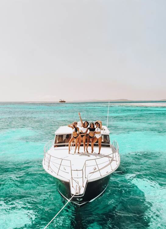 Three women enjoying a sunny day on a boat in the ocean, surrounded by blue water and clear skies.