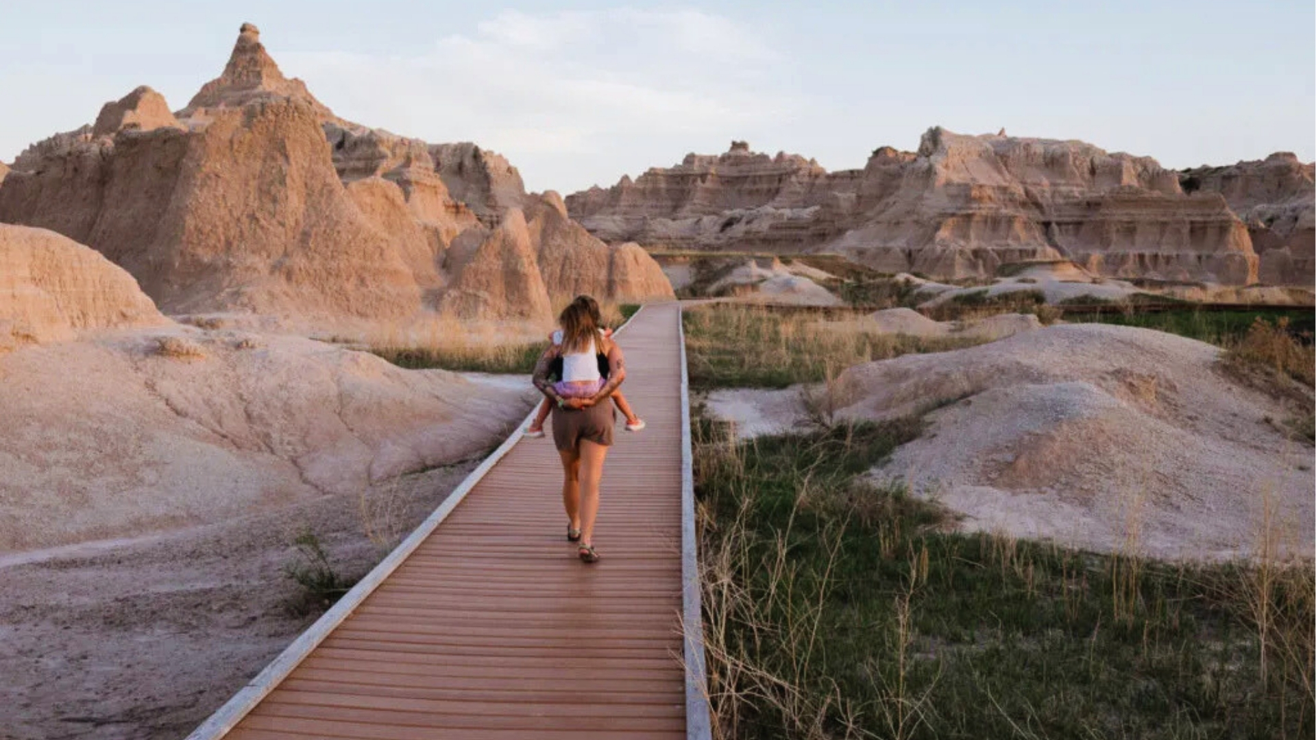 A woman walks along a wooden walkway, surrounded by the rugged landscape of the badlands.