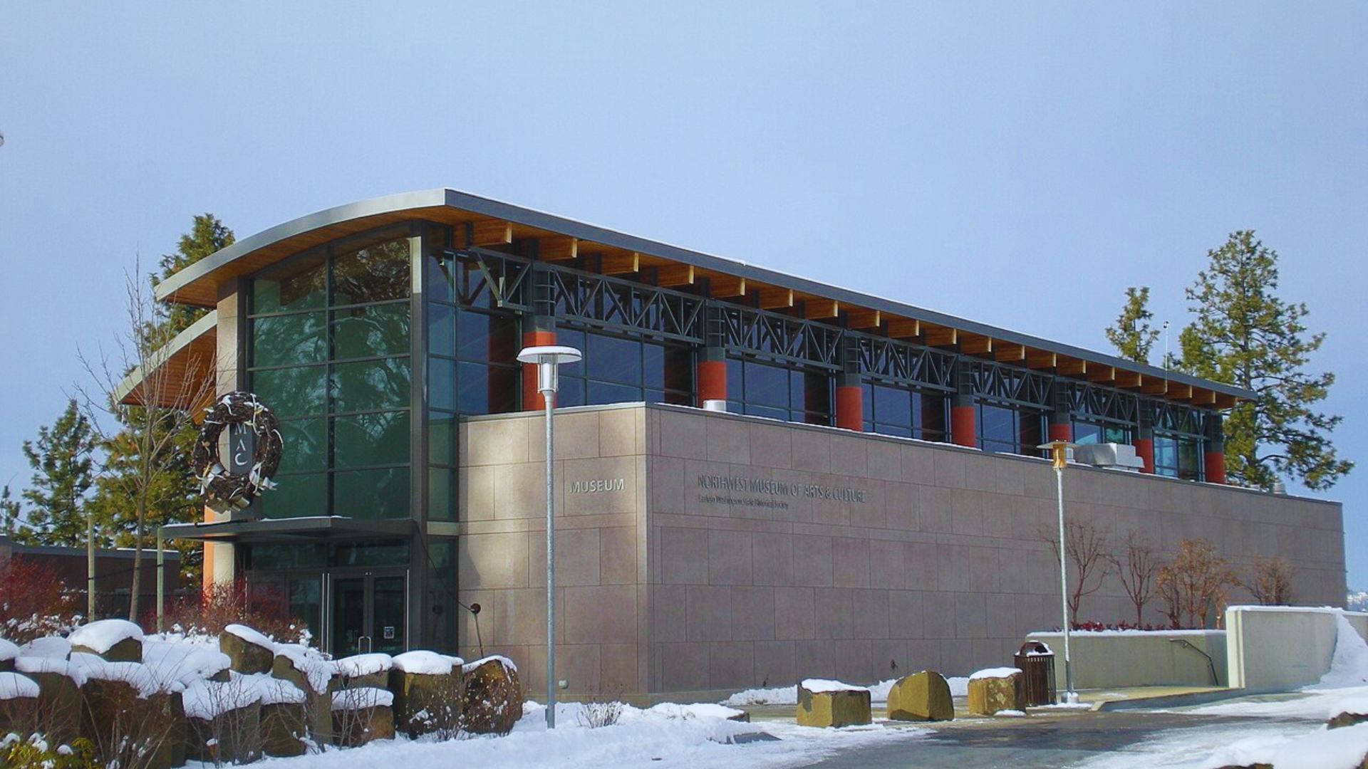 A modern building featuring a large glass wall, surrounded by a blanket of snow on the ground.