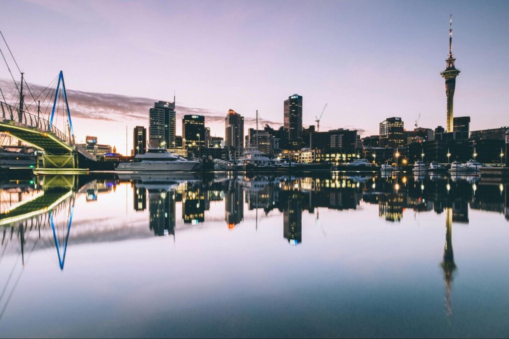 Auckland city skyline illuminated at dusk, showcasing tall buildings against a colorful twilight sky.