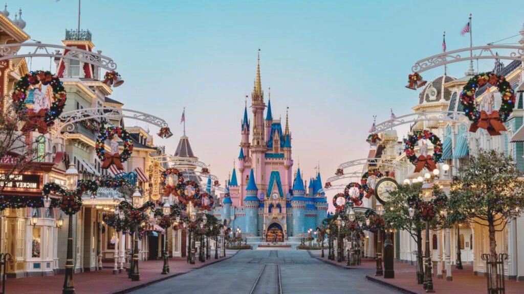 Main Street at Disney World, adorned with festive holiday wreaths and garlands, leads to a colorful Cinderella Castle under a clear, pastel sky.