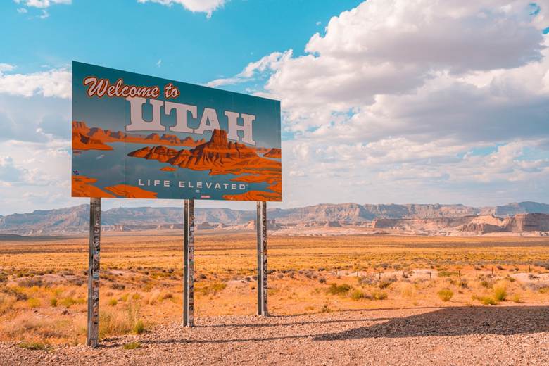 Utah welcome sign featuring mountains and the state name in bold letters against a blue sky background.