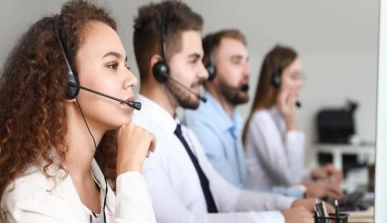 A diverse group of people working together in a busy call center, each at their own workstation with headsets.