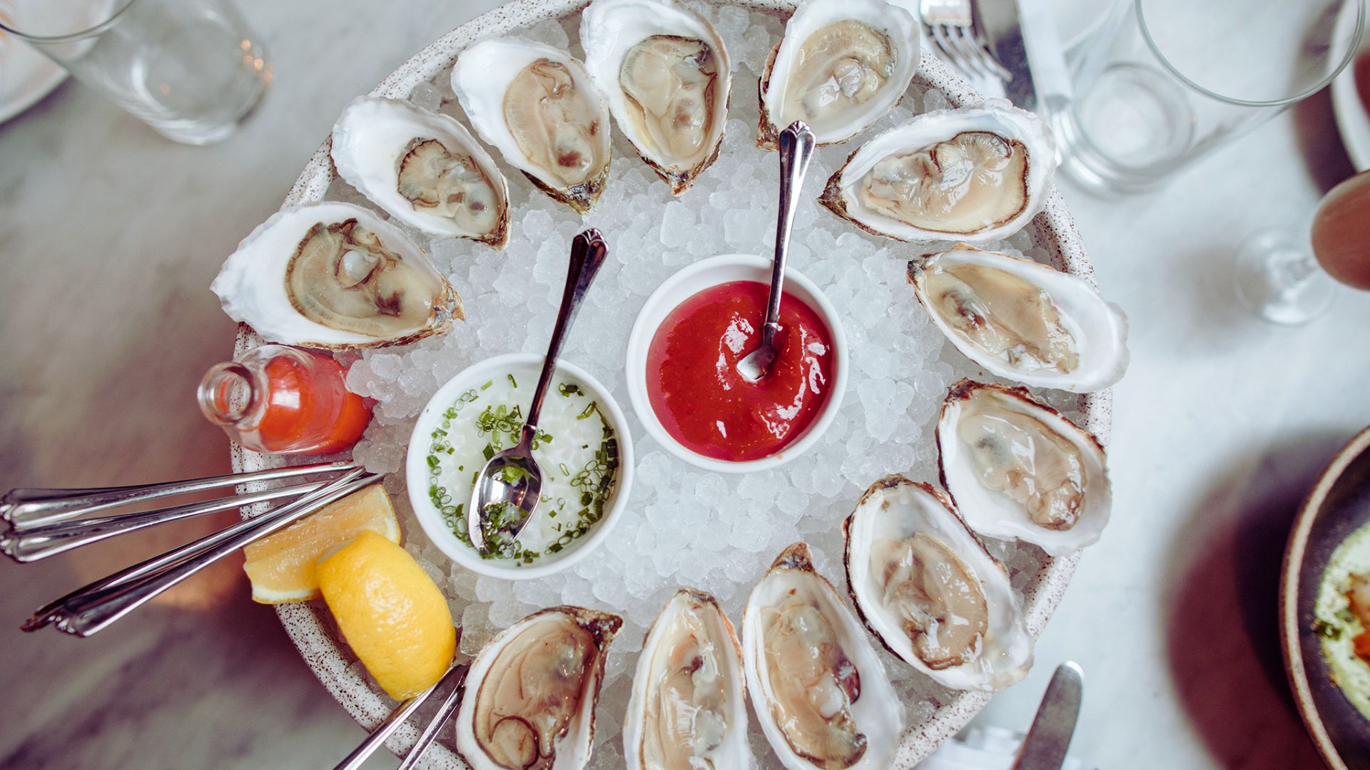 Fresh oysters on the half shell arranged on a plate with lemon wedges and cocktail sauce.
