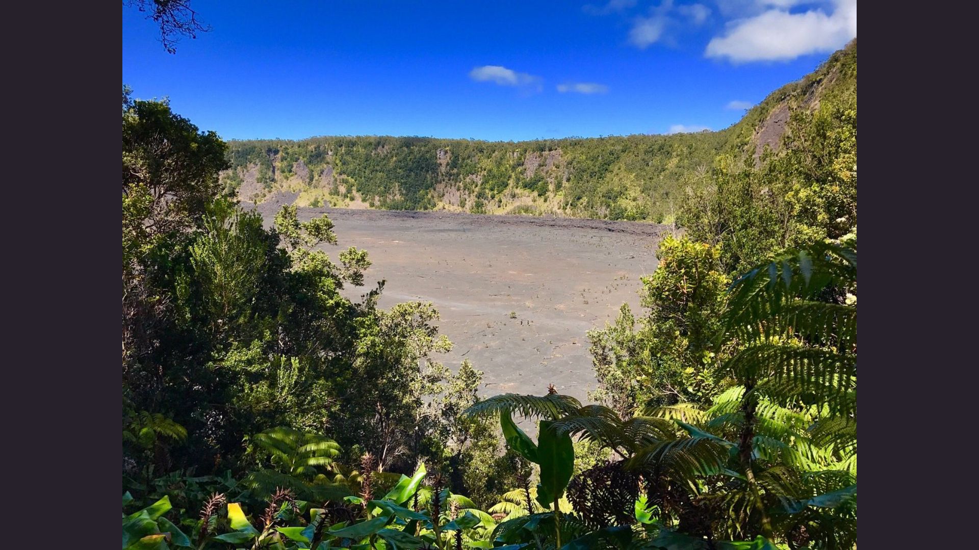 A panoramic view of a lava crater from the summit of a mountain, showcasing the rugged terrain and volcanic landscape.