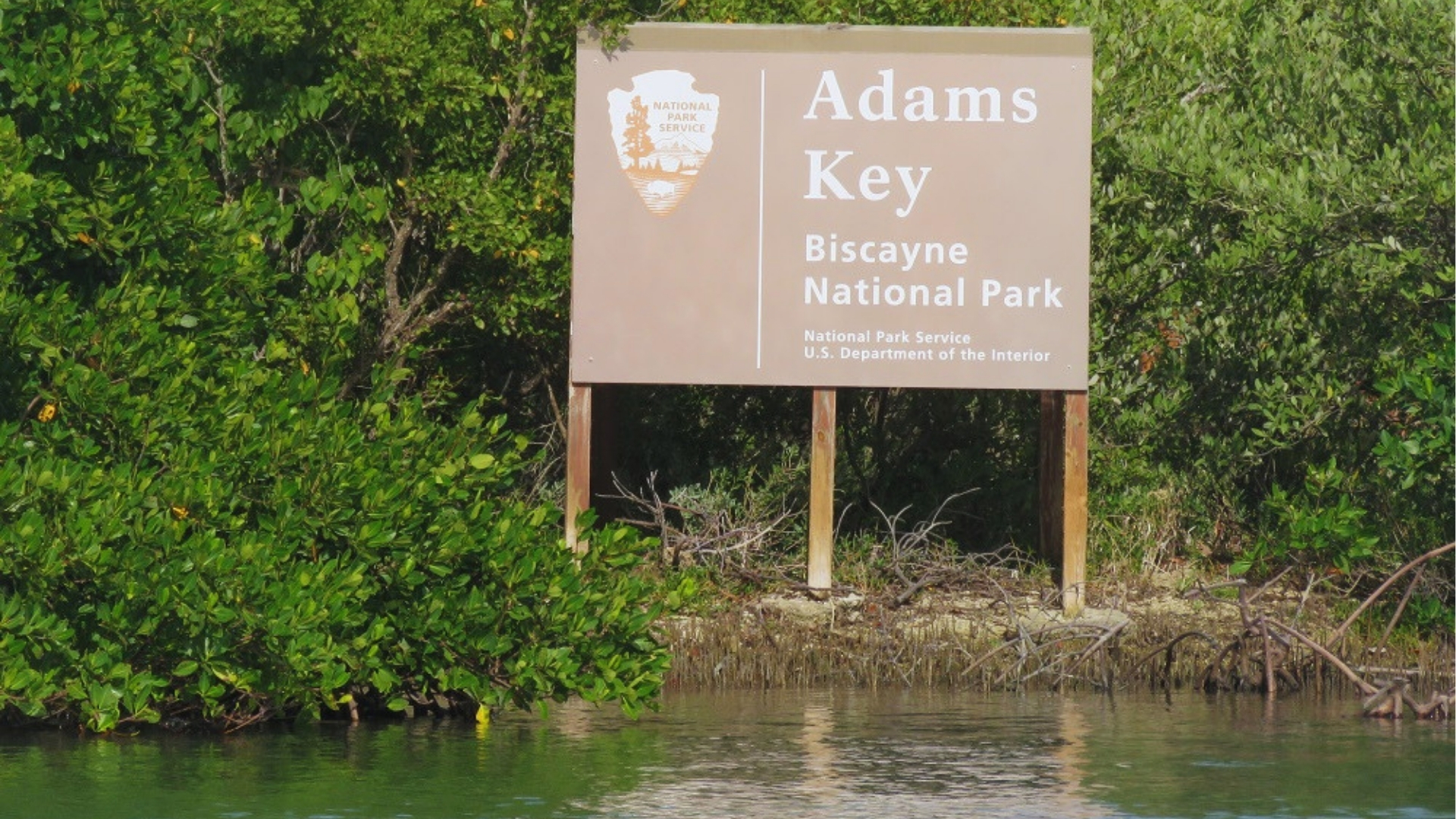 Sign for Adams Key in Biscayne National Park, surrounded by lush green mangroves and calm water, conveying a serene, natural atmosphere.