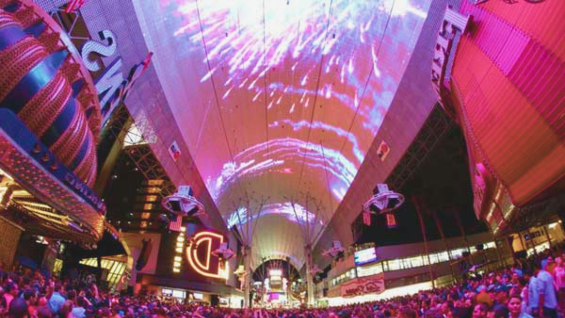 A bustling crowd gathers in a city at night, illuminated by streetlights and vibrant city lights.