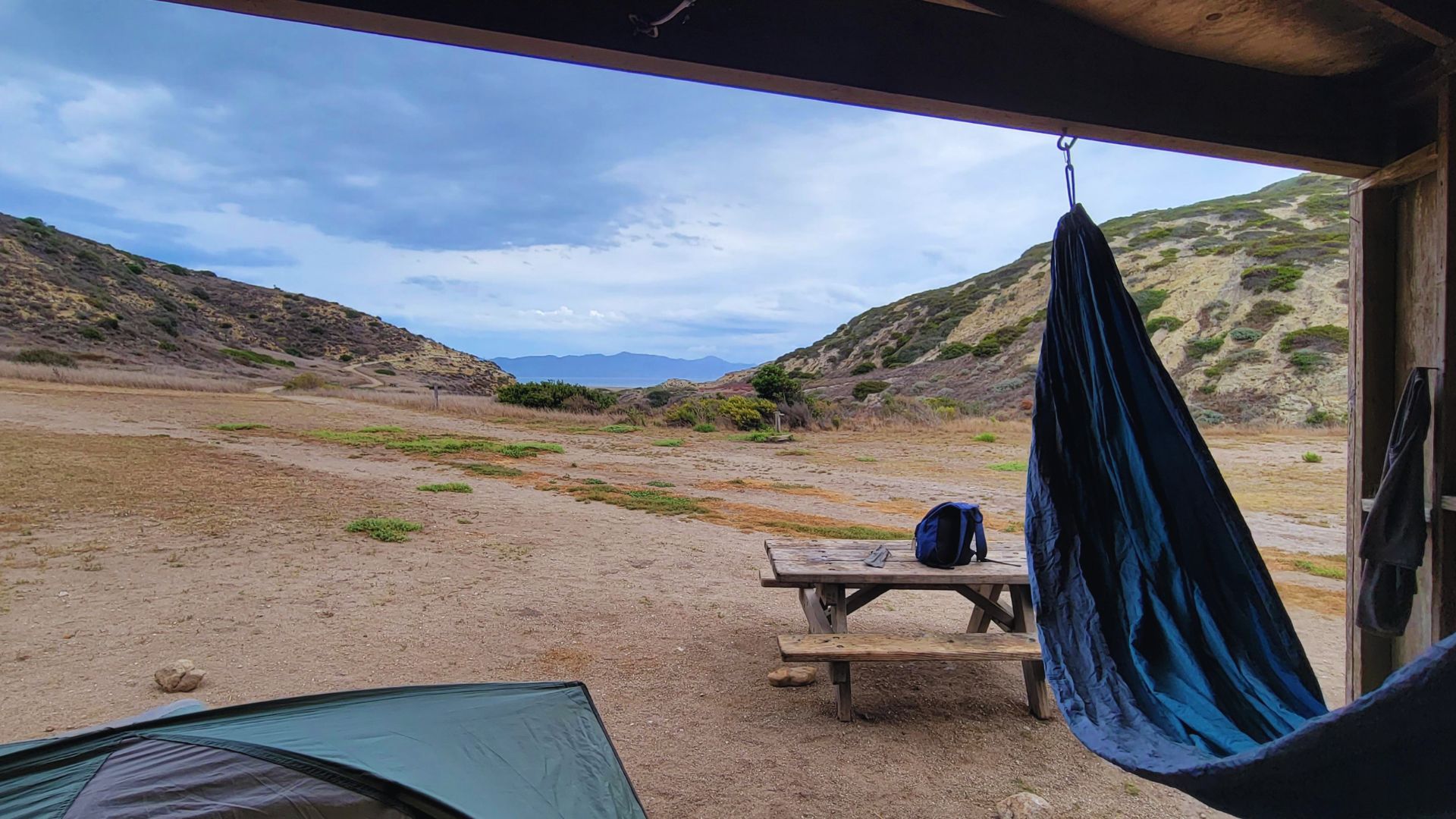 A hammock is suspended from a tent in a vast desert landscape under a clear blue sky.