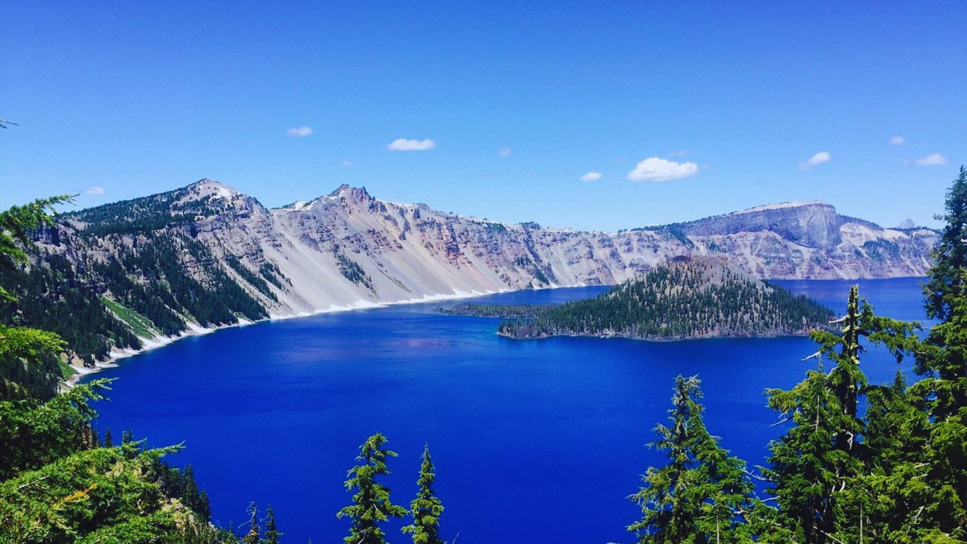 Crater Lake National Park in Oregon, showcasing deep blue water surrounded by steep cliffs and lush forested areas.