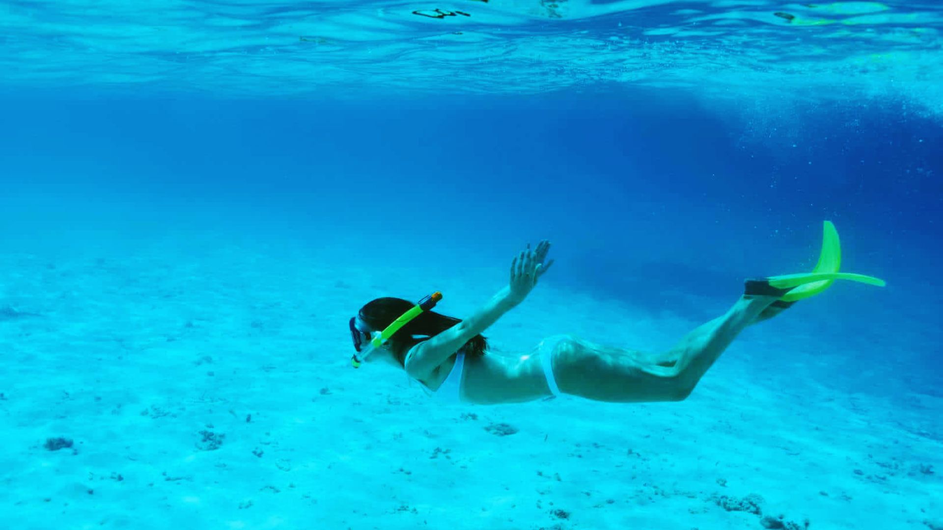A snorkeler in clear blue water, wearing fins and a snorkel, gracefully swims near the ocean floor. The scene conveys a sense of tranquility and exploration.
