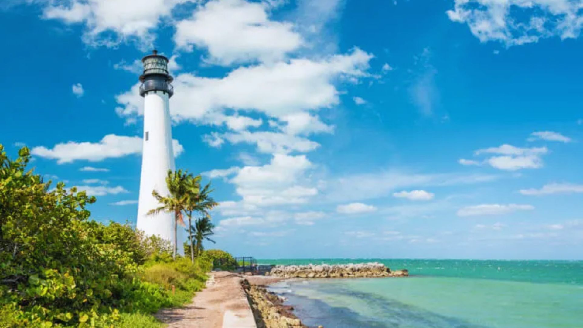 A tall lighthouse stands on the shoreline, overlooking the ocean waves under a clear blue sky.