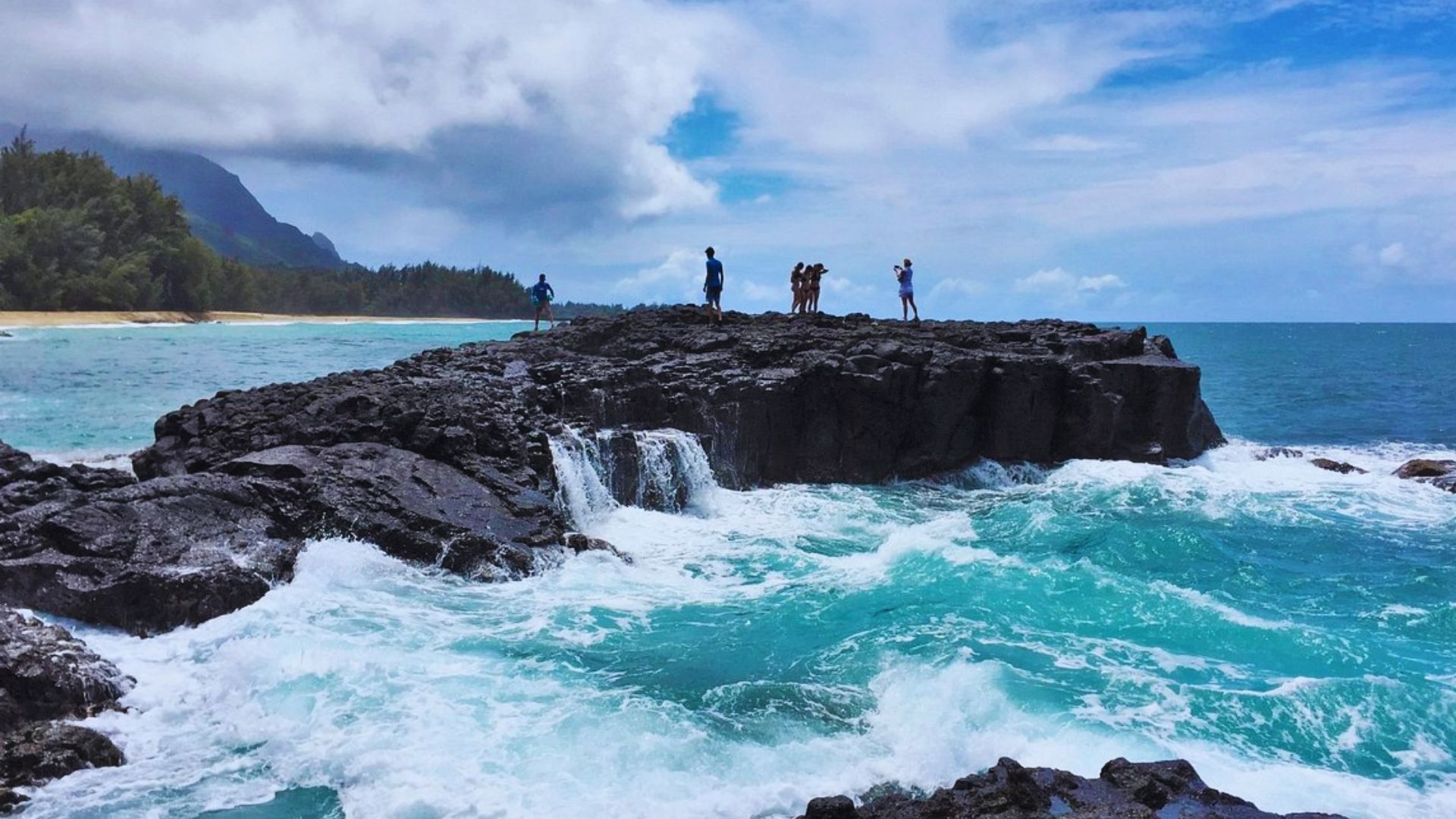 A group of people standing on rocky outcrops, gazing out at the vast ocean under a clear blue sky.