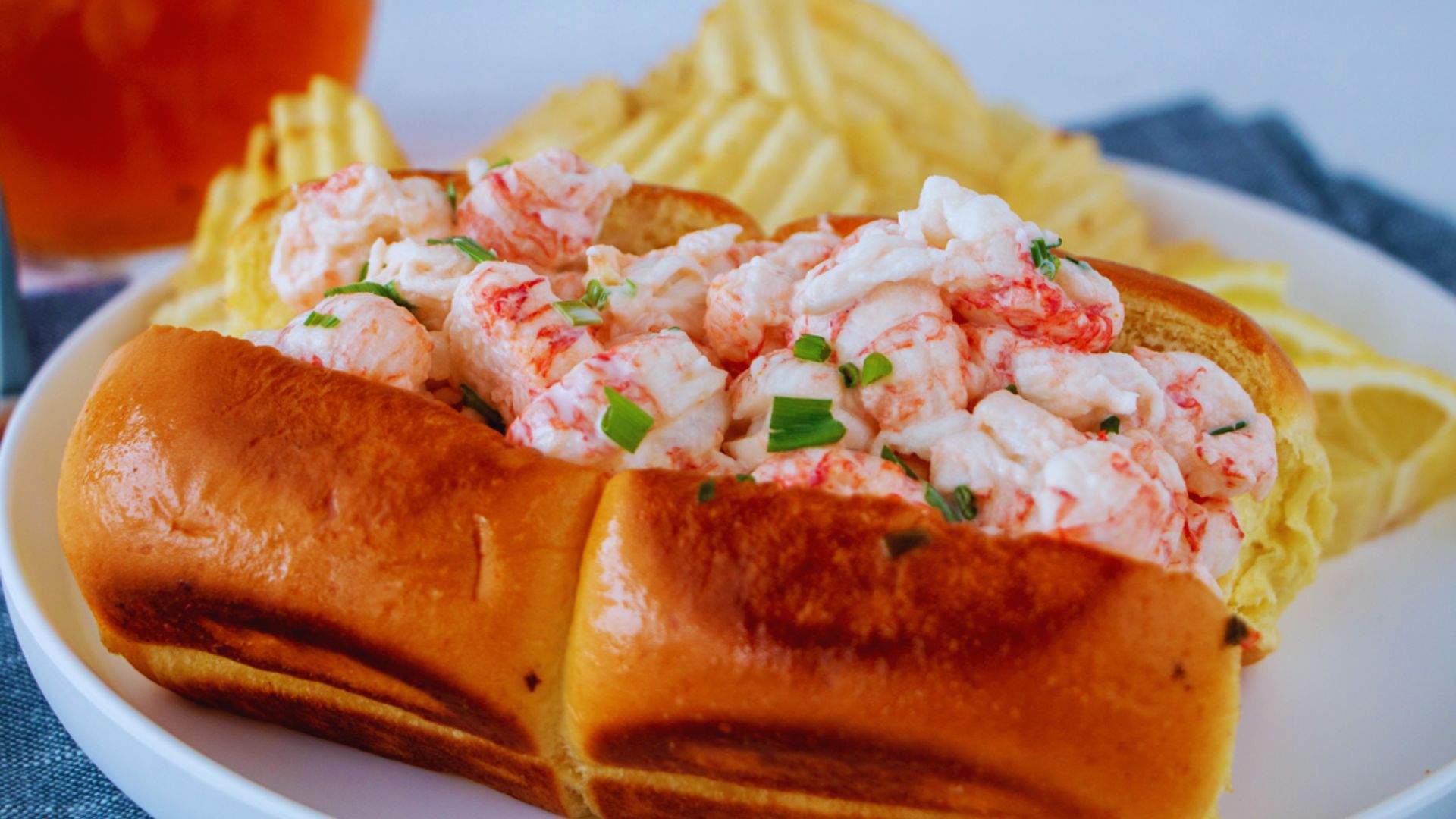 A lobster roll served on a plate alongside crispy chips and a cold beer.