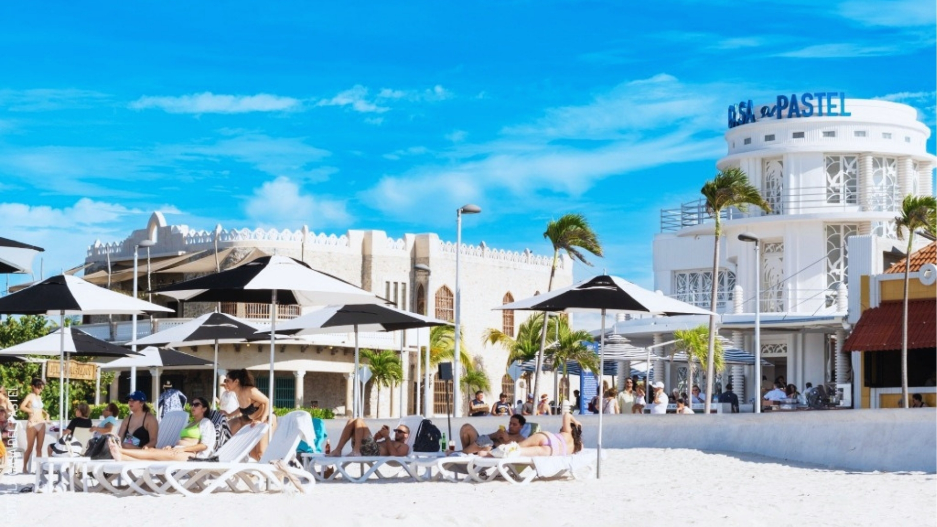 A sunny beach scene featuring colorful umbrellas and lounge chairs arranged on the warm sand.