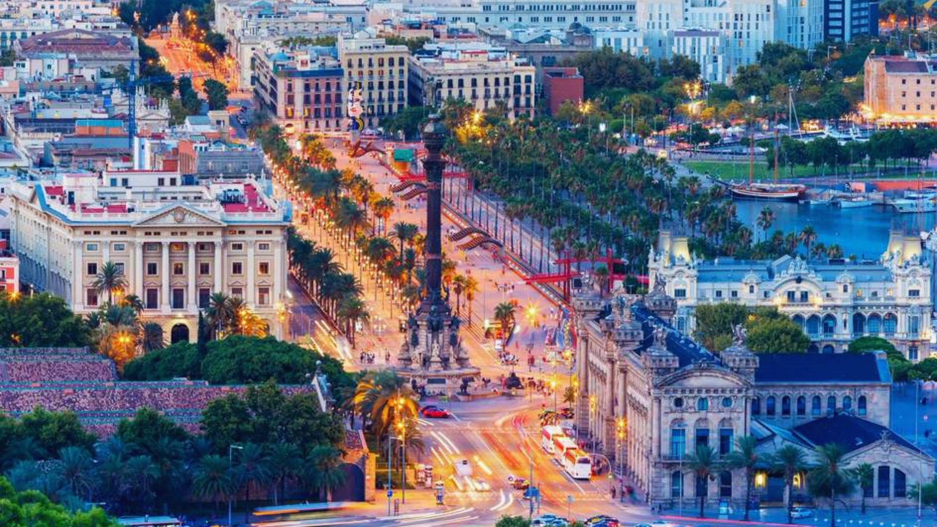 Aerial view of a vibrant cityscape at dusk, featuring a bustling boulevard lined with palm trees, historic buildings, and glowing streetlights.