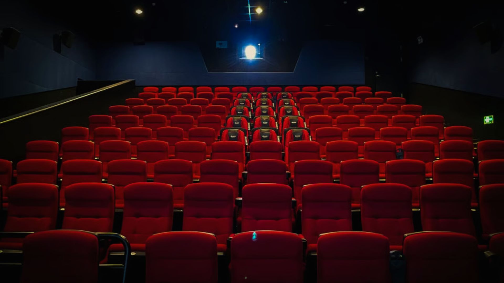 Empty movie theater with rows of vibrant red seats and a large screen. The dim lighting and focused spotlight create a sense of anticipation.