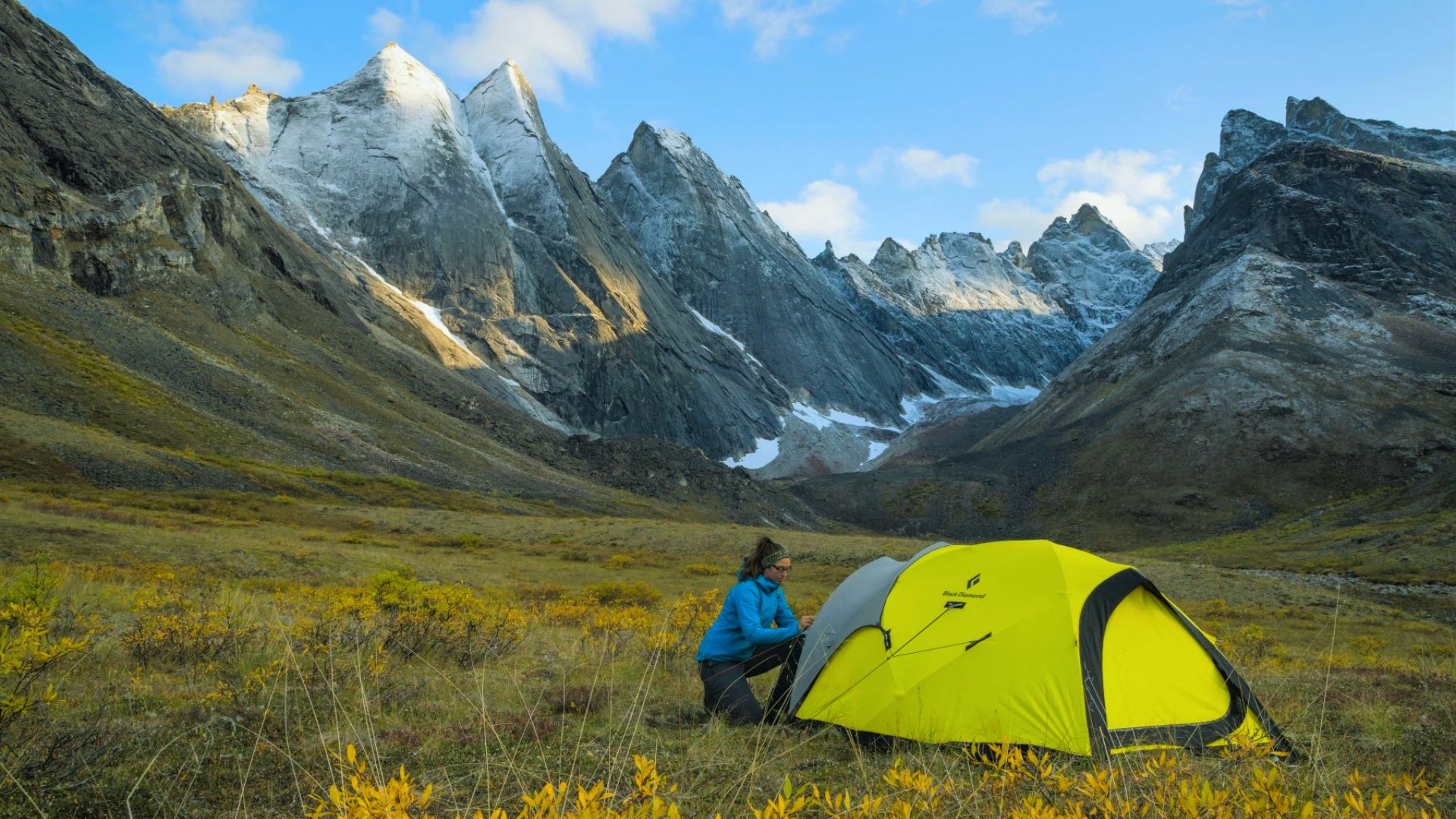 A person is setting up a tent with majestic mountains in the background, preparing for an outdoor adventure.