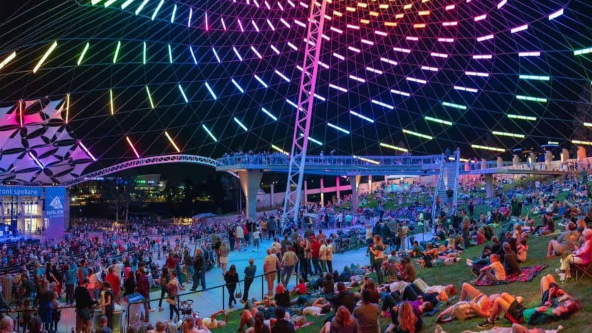 A large crowd of people sitting on grass at night, illuminated by soft lights, creating a festive atmosphere.