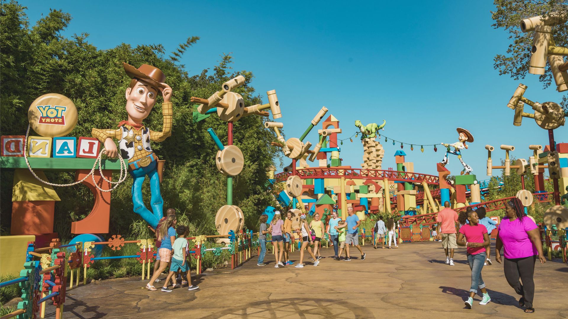 Alt text: "Theme park entrance resembling a colorful toy land with oversized toy figures and blocks. Families and children walk around, excited and playful."