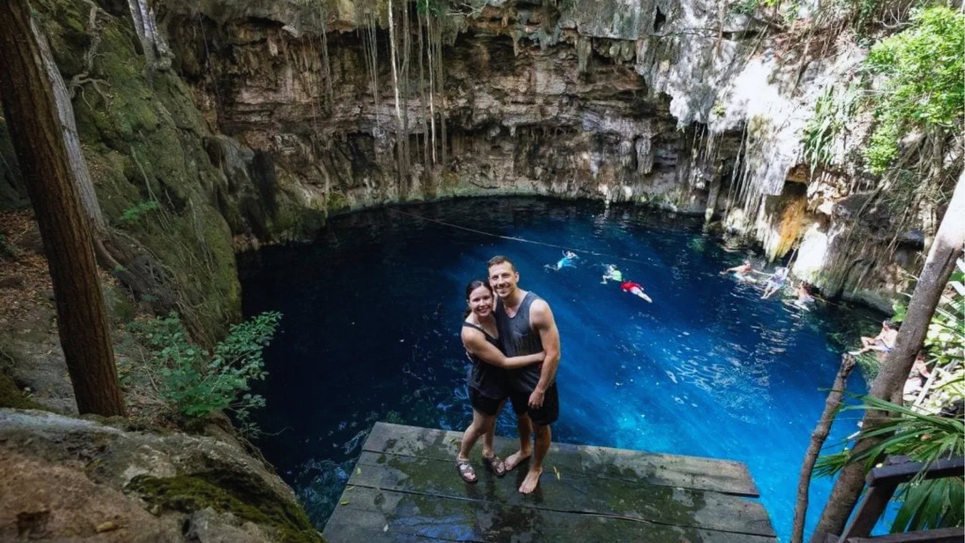 Couple standing on steps, smiling, with a stunning blue hole visible in the background.