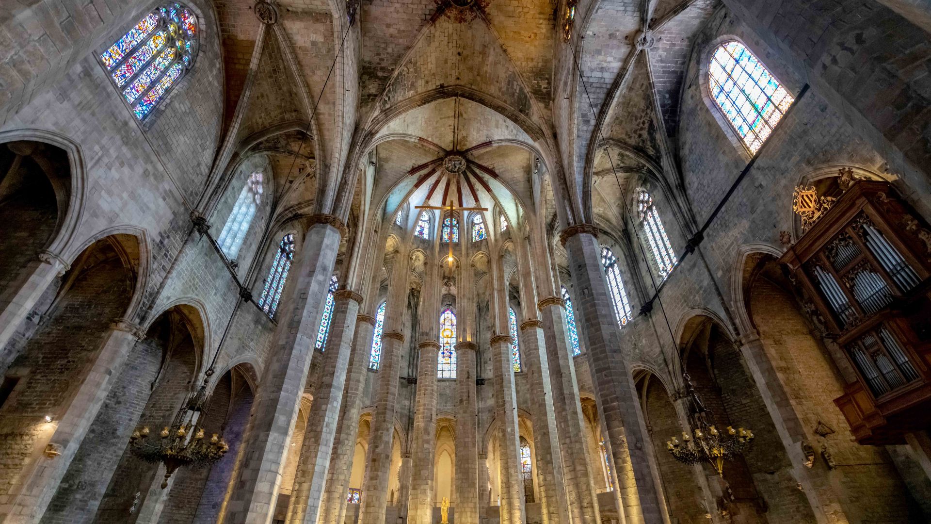 Interior of a grand Gothic cathedral, featuring tall stone columns, ribbed vaults, and colorful stained glass windows. The scene conveys awe and reverence.