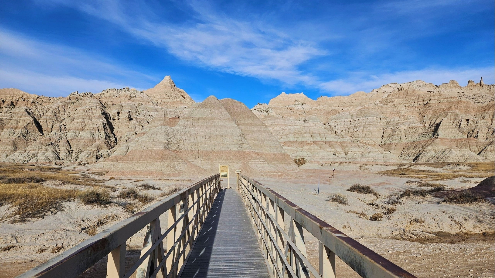 A wooden bridge extends towards the rugged terrain of Badlands National Park, showcasing its unique geological formations.