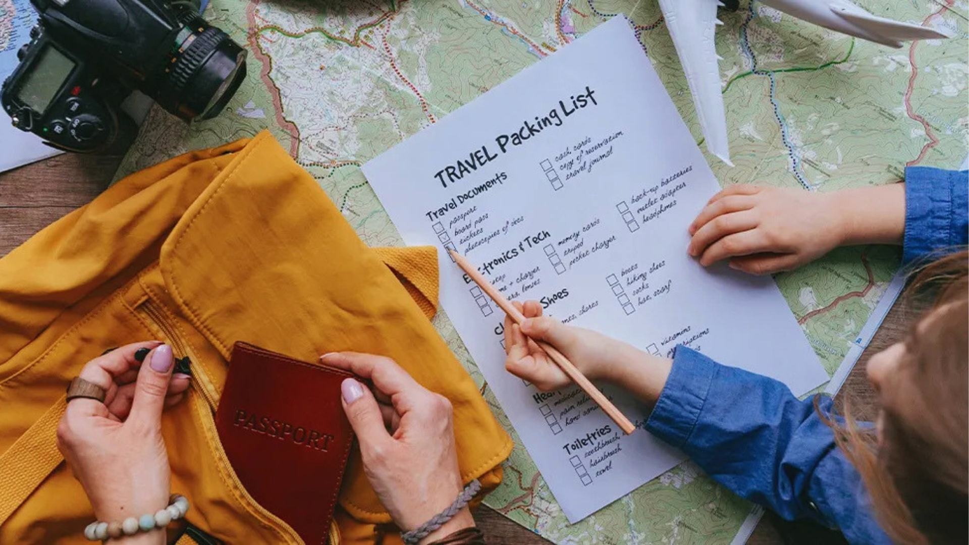A person and a child prepare for travel, checking items on a packing list. Nearby are a camera, a passport, a yellow bag, and a map, conveying excitement.