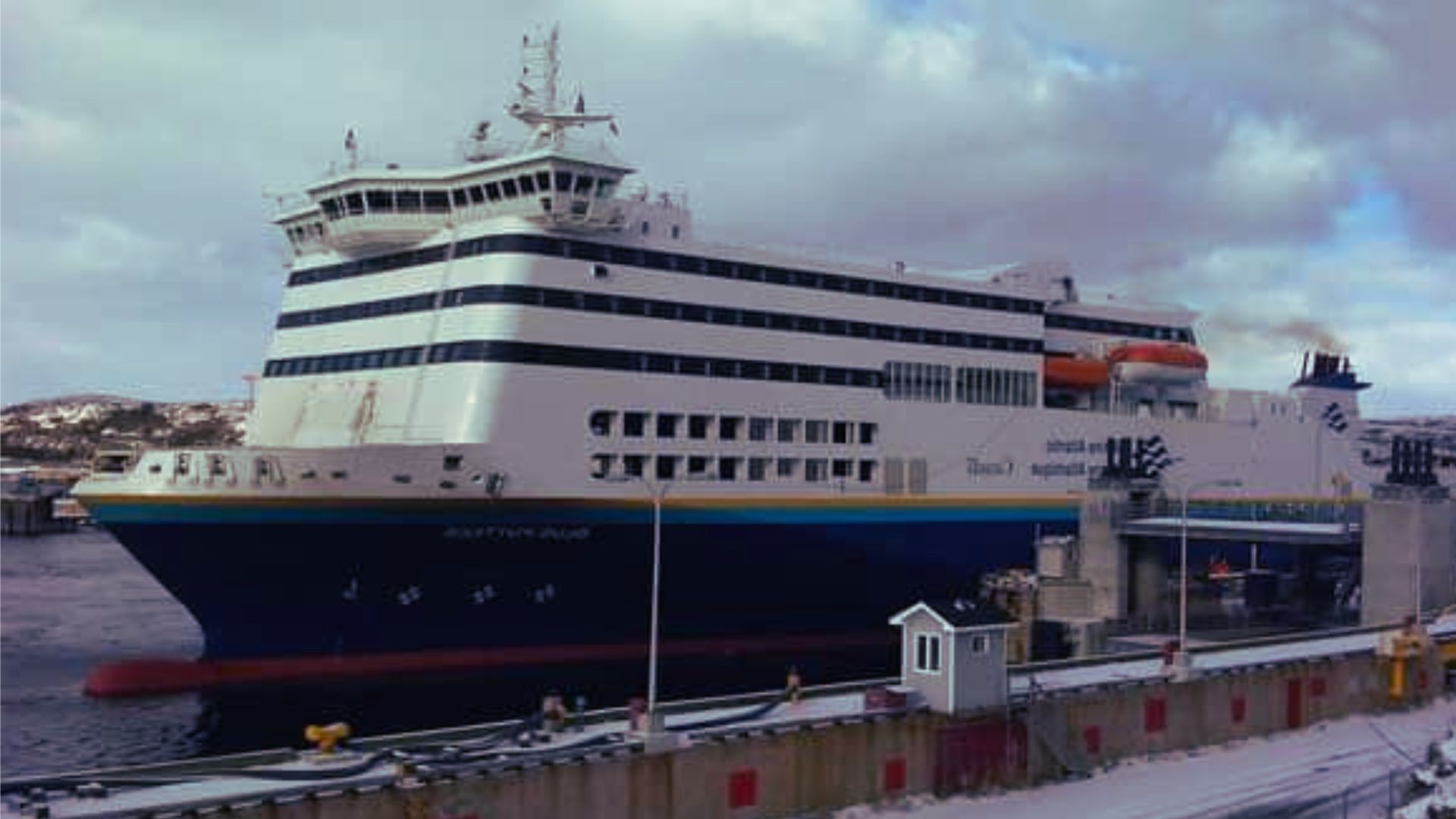 A large ferry is docked at a snowy dock, surrounded by a winter landscape.