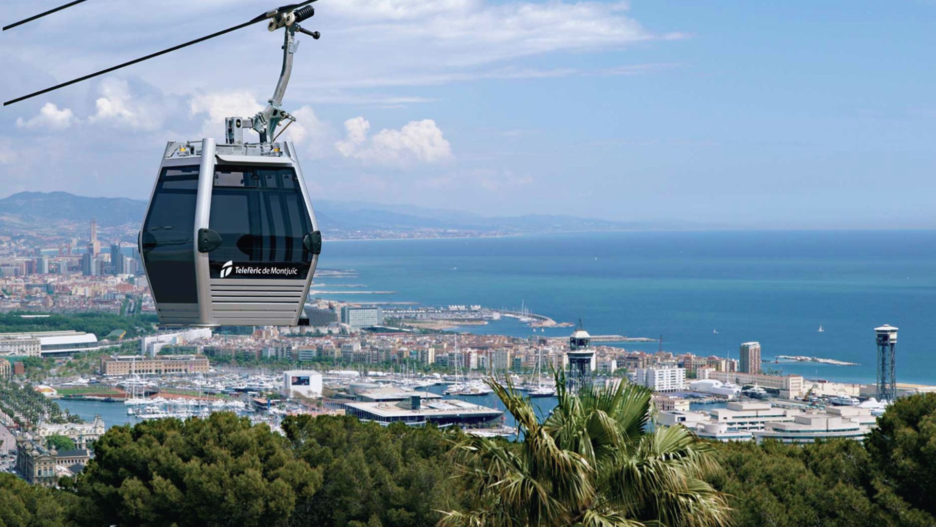 A cable car labeled "Telefèric de Montjuïc" glides above lush greenery, overlooking a bustling coastal cityscape and serene blue sea under a clear sky.