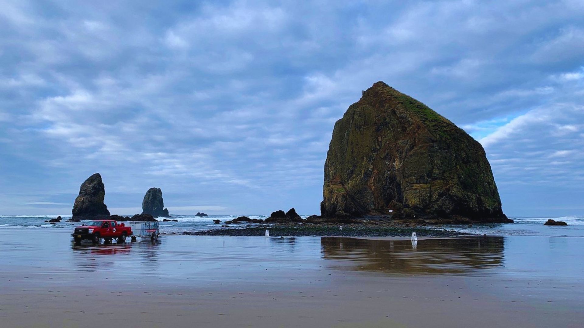 Haystack Rock rises majestically at Cannon Beach, Oregon, surrounded by sandy shores and ocean waves under a clear sky.
