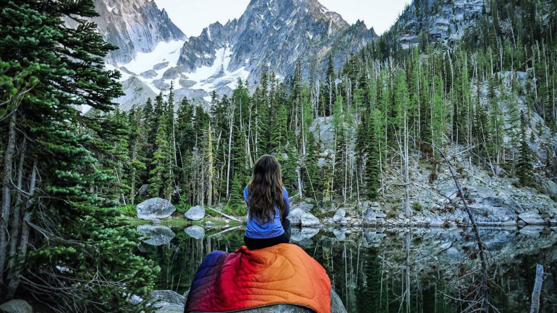 A woman sits on a rock, draped in a blanket that covers her head, creating a cozy and contemplative atmosphere.