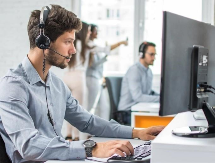 A man wearing headphones sits at a desk in an office, focused on his work.