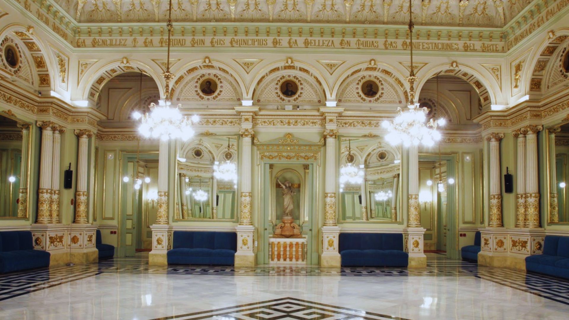 Ornate ballroom with elegant chandeliers, detailed gold trim, and arched mirrors. Blue velvet seating adds luxury to the polished marble floor.