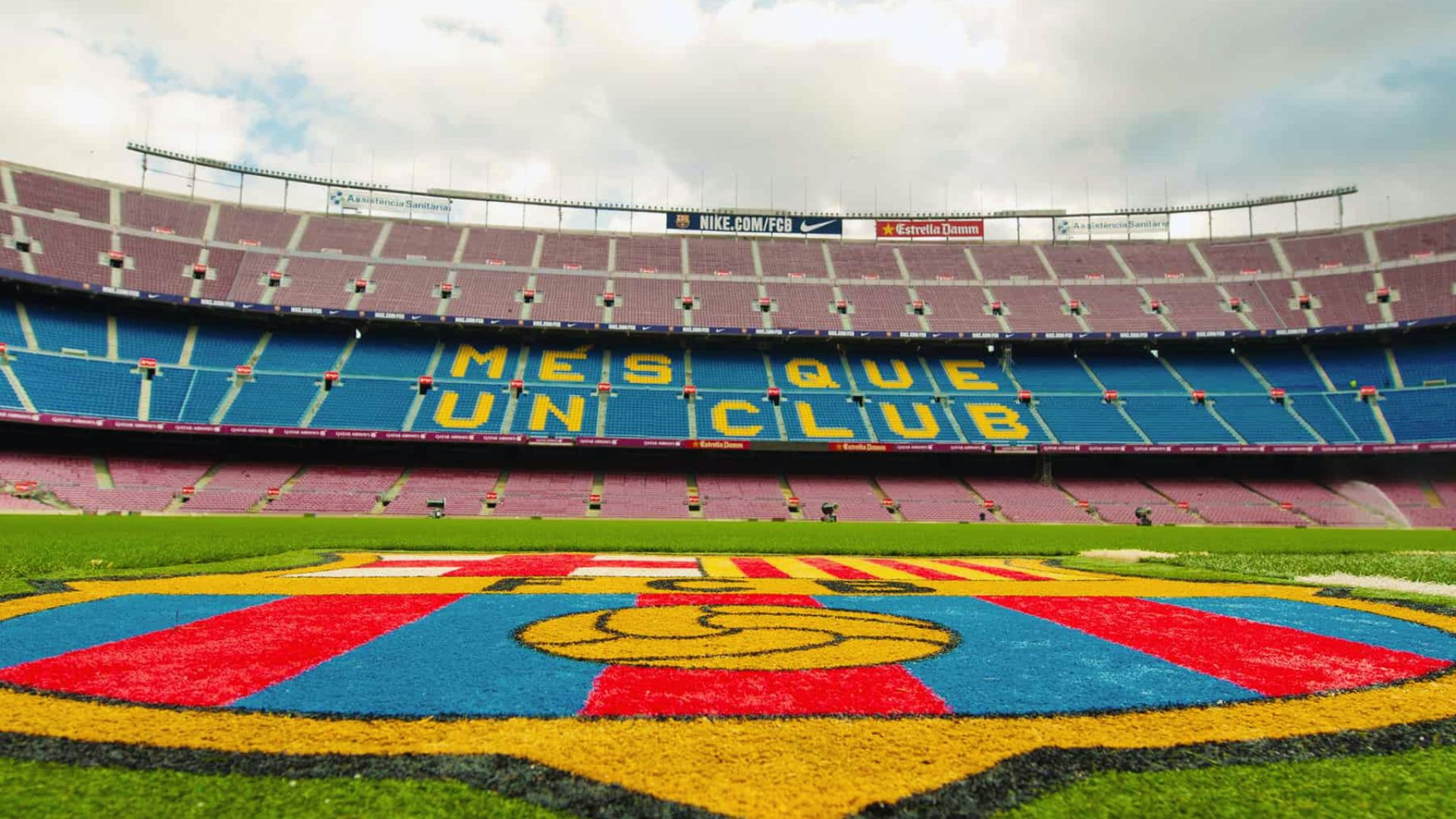 The image shows a large football stadium with pink and blue seats, displaying the words "Mes Que Un Club." The foreground features a vibrant team crest.