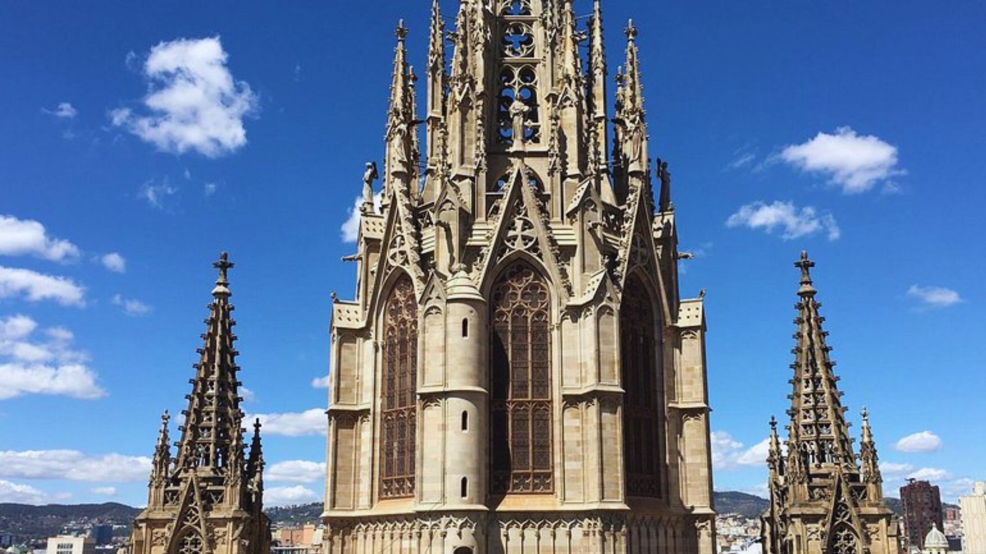 Gothic cathedral with intricate spires and stained glass windows, set against a clear blue sky with scattered clouds. The scene conveys grandeur and serenity.