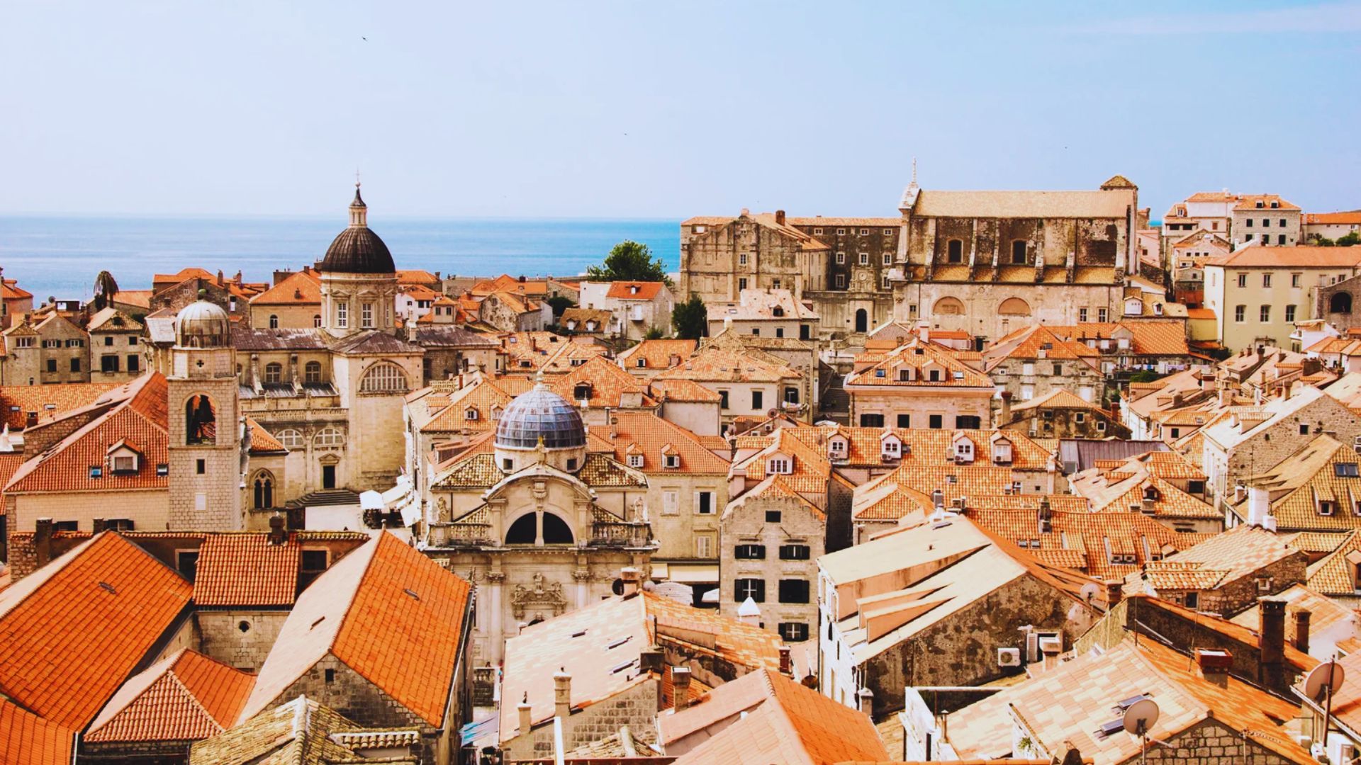Rooftop view of Dubrovnik, Croatia, featuring terracotta tiles and historic stone buildings. The scene conveys a warm, historic Mediterranean vibe.