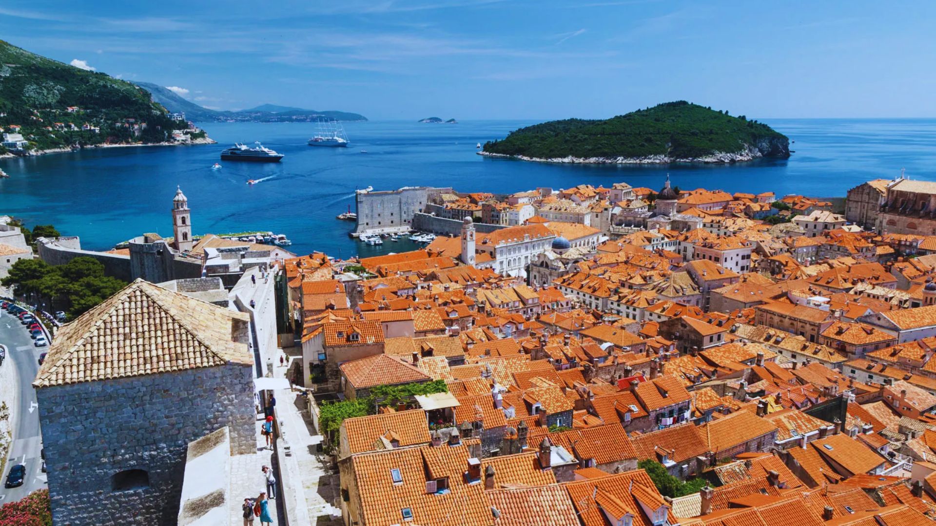 Rooftop view of Dubrovnik's Old Town, showcasing vibrant orange terracotta roofs, historic stone buildings, and the bright blue Adriatic Sea.