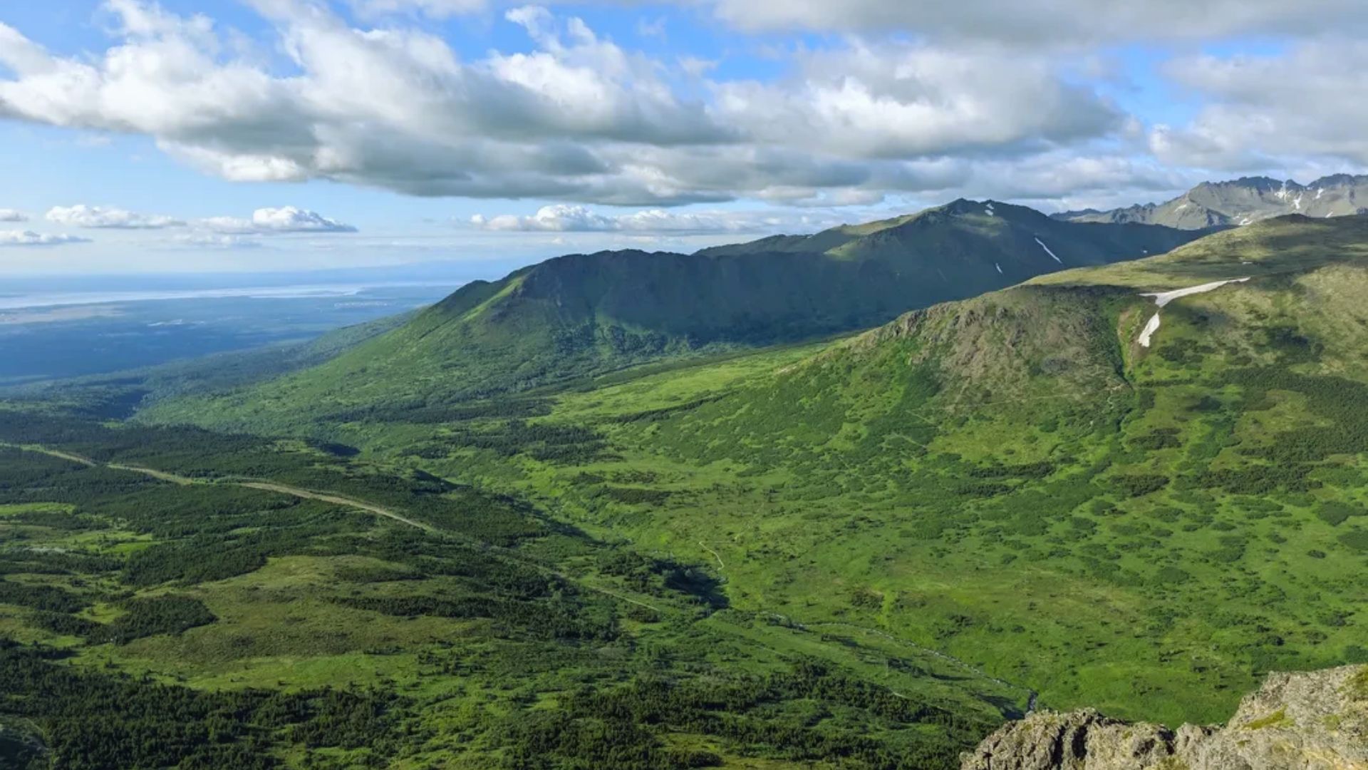 A panoramic view of mountains and valleys from a mountain top, showcasing lush greenery and rugged terrain below.