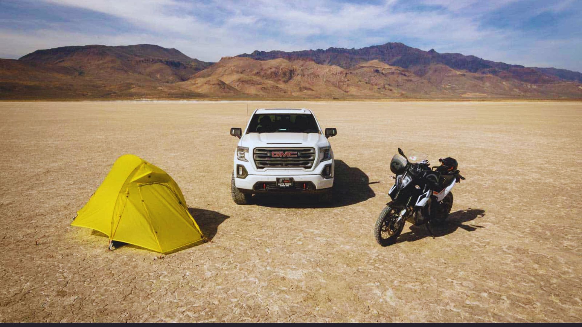 A white truck and a motorcycle parked on a sandy desert landscape under a clear blue sky.
