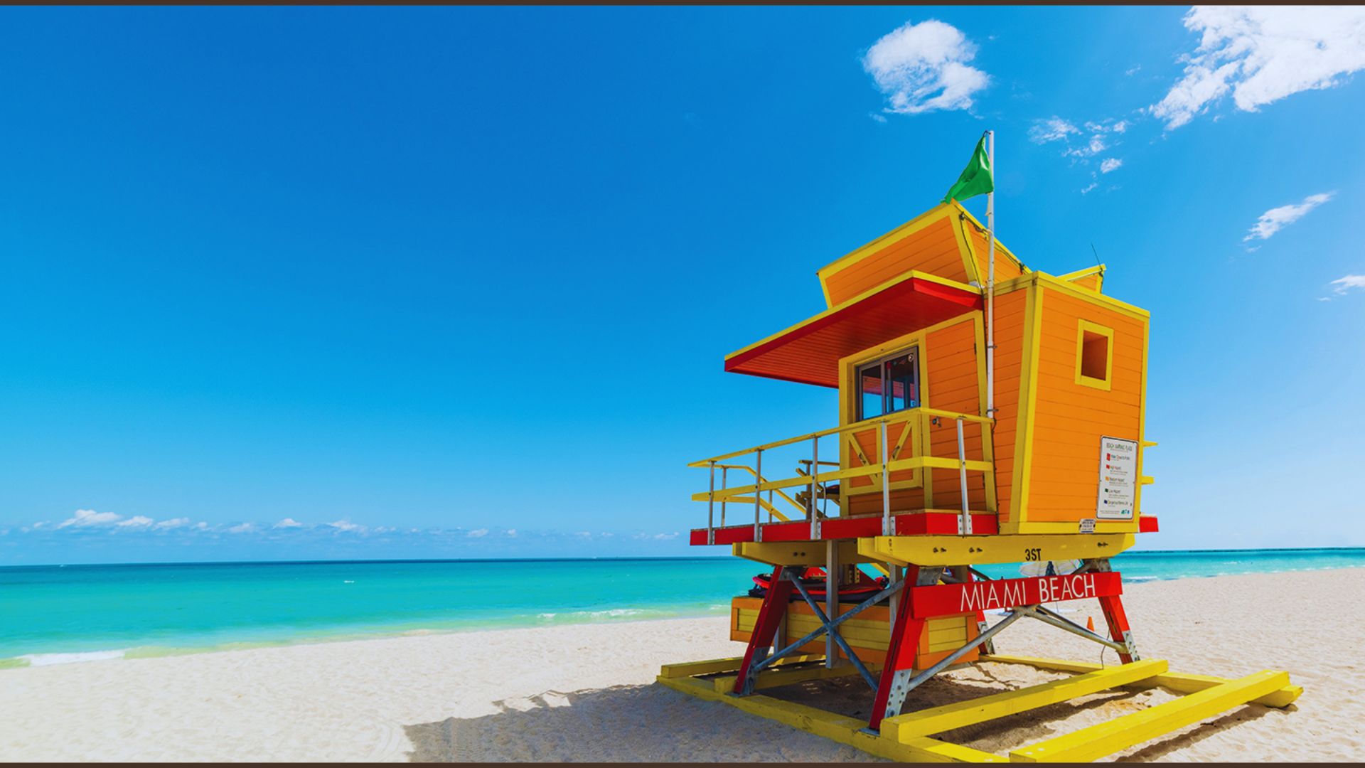 Vibrant yellow and red lifeguard tower on Miami Beach with clear blue skies and turquoise ocean, conveying a sunny and cheerful vibe.
