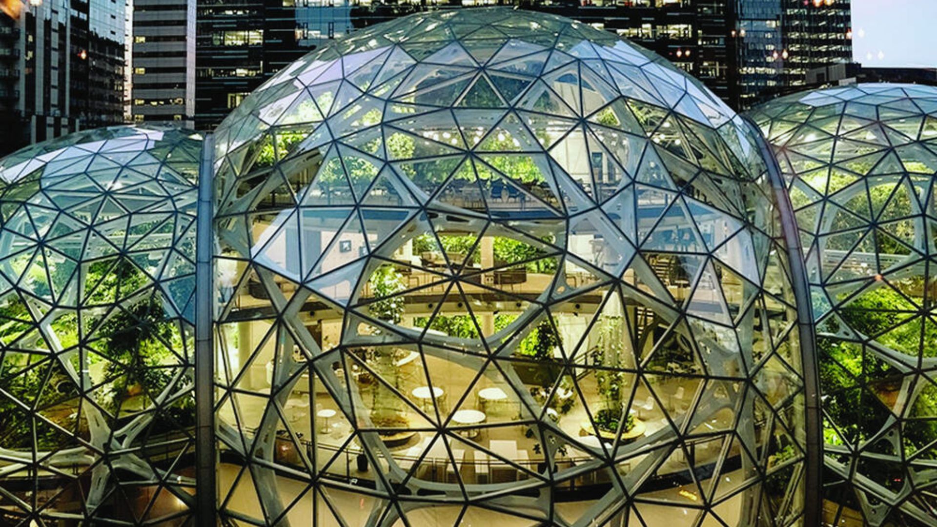The image shows a glass geodesic dome of an urban greenhouse filled with lush greenery, surrounded by city buildings, conveying a blend of nature and modernity.