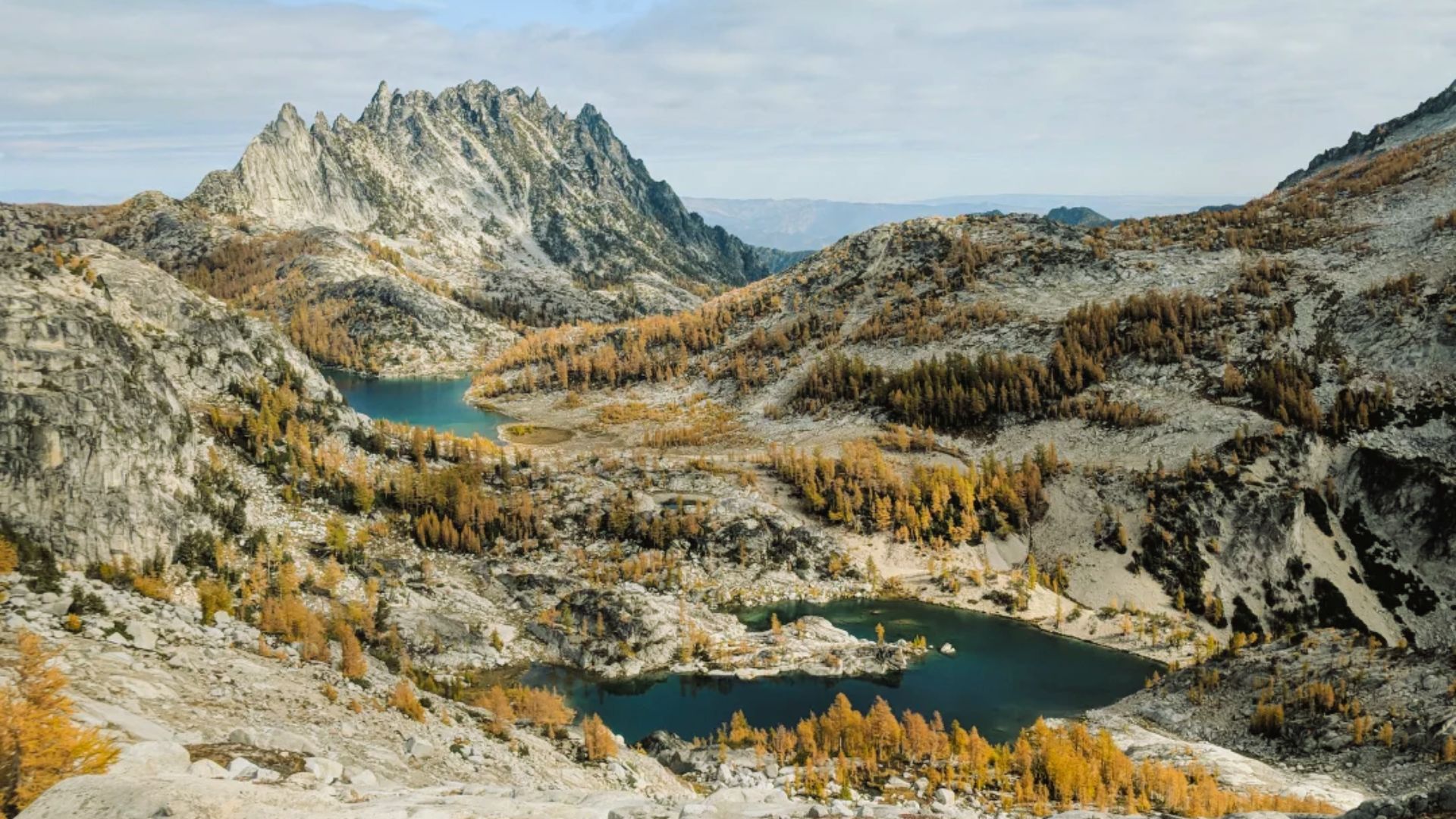 A panoramic view from a mountain peak showcasing vibrant fall foliage and distant valleys under a clear blue sky.
