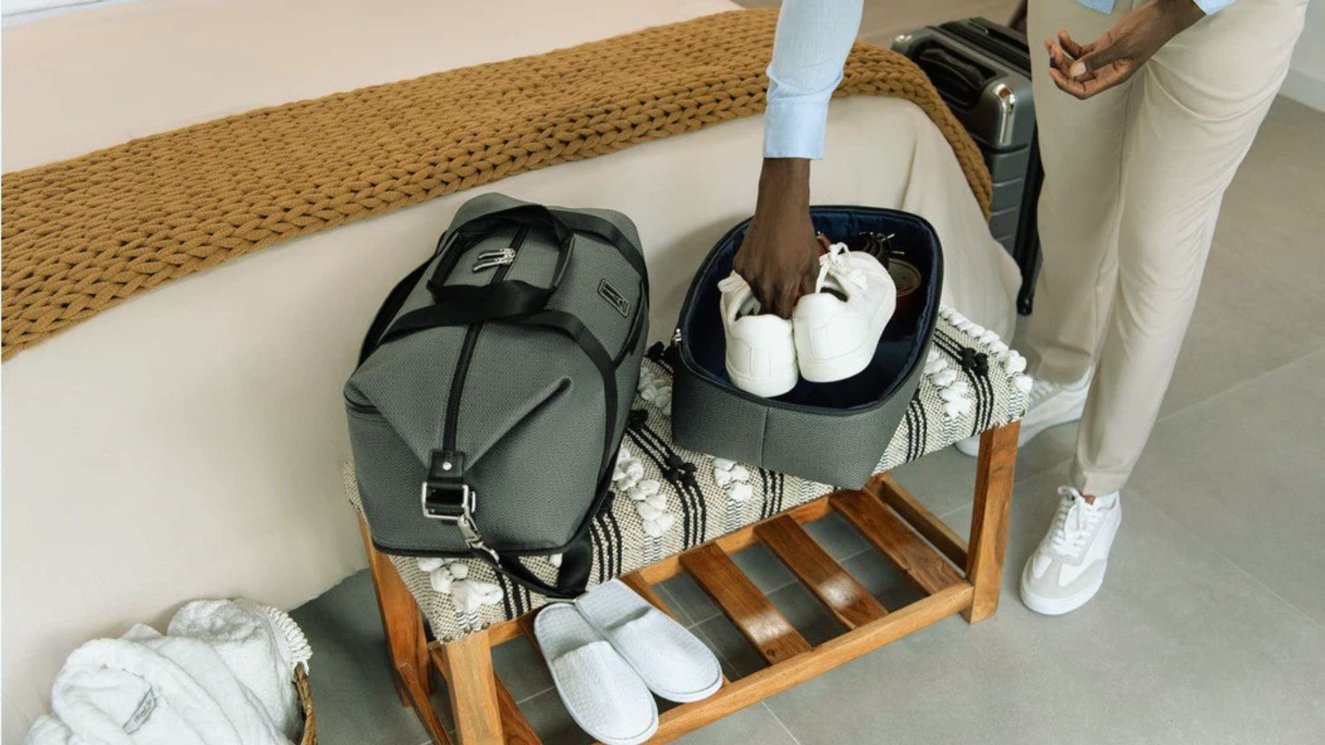 A man is placing his luggage into an open suitcase, preparing for travel.
